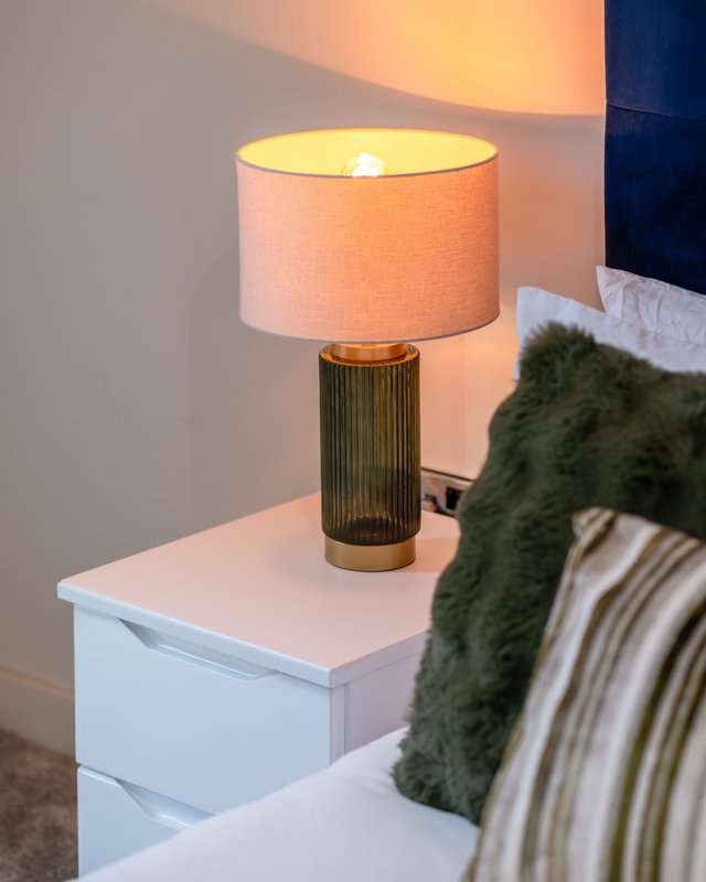 Bedside table with brass table lamp, pink shade, and green cushion on bed