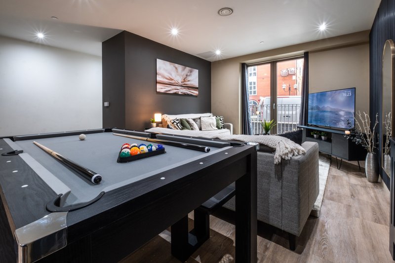 Modern games room with pool table, grey armchair, bed, and wall-mounted TV