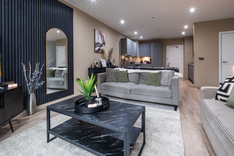 Modern open-plan living room with gray sofa, black marble coffee table, kitchen area, and designer lighting