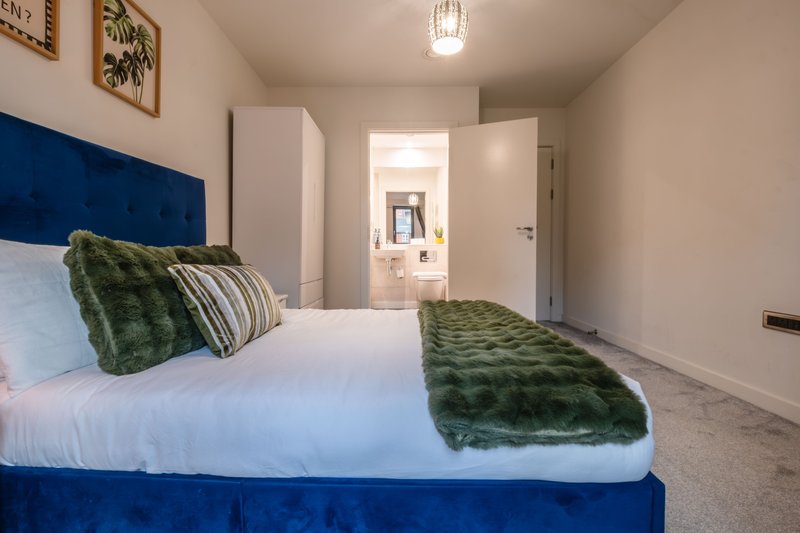 Bedroom with double bed, blue headboard, green cushions and throw, ensuite visible through doorway