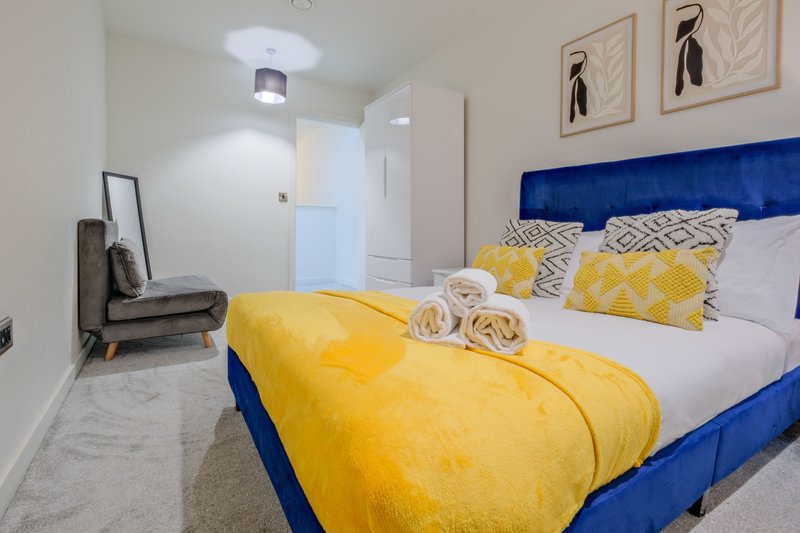 Modern bedroom with blue upholstered bed, yellow bedding, patterned cushions and wall art
