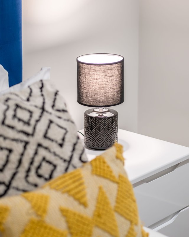 Bedside table with textured lamp, patterned cushions and throw blanket