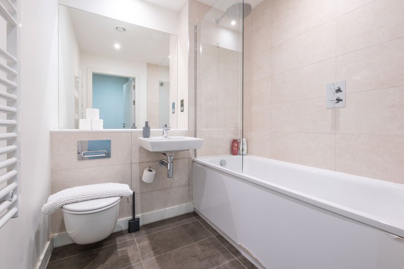 Modern bathroom with wall-mounted toilet, sink, bathtub, large mirror and glass shower screen