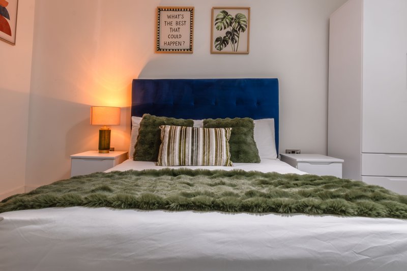 Bedroom with blue upholstered headboard, green bedding, striped pillows, and bedside lamp