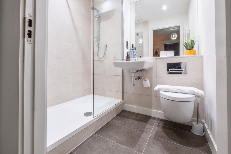 Modern bathroom with walk-in shower, white sink, toilet, and dark tile flooring