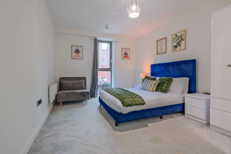 Modern bedroom with blue upholstered bed, white furniture, armchair, and framed wall art
