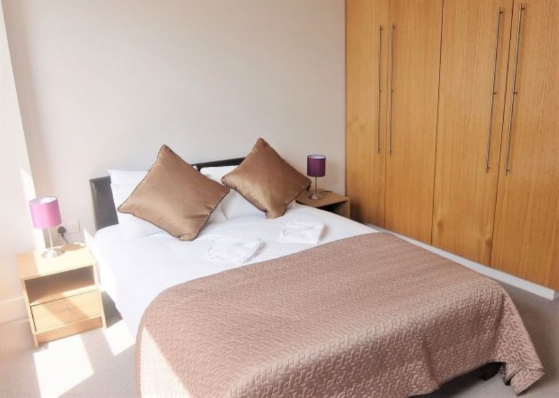 Bedroom with double bed, brown cushions, wooden wardrobe and bedside table