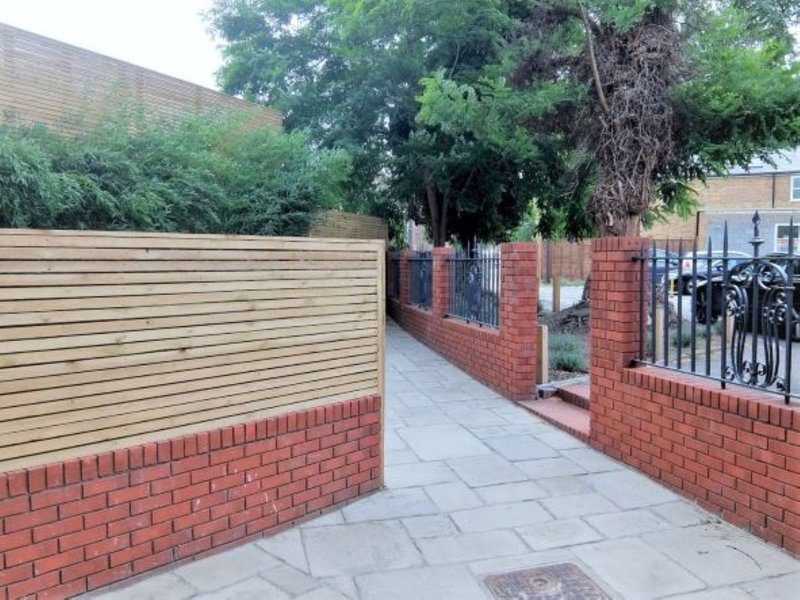 Exterior driveway with brick walls, wooden fence, paved surface and mature trees