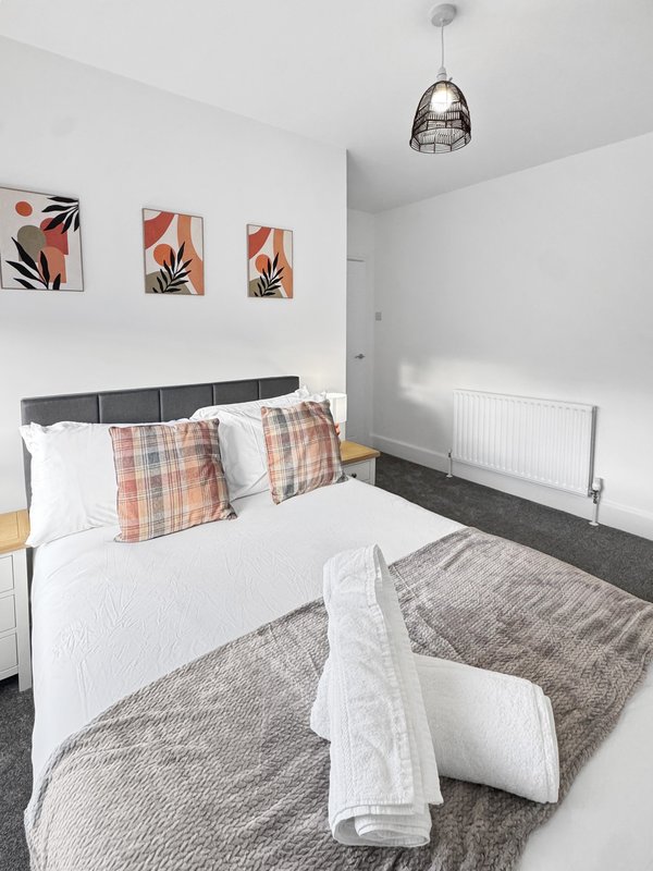 Modern bedroom with double bed, plaid cushions, white bedding, pendant light and wall art