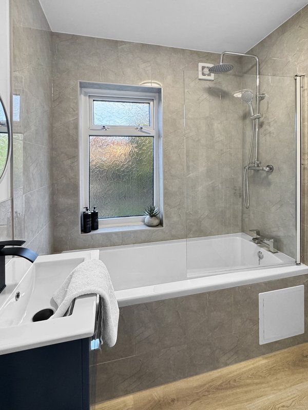 Modern bathroom with white bathtub, shower enclosure, window and wooden floor