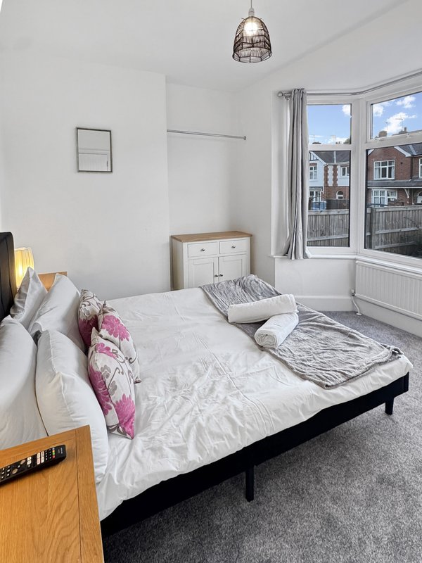 Bright bedroom with double bed, white bedding, pendant light, and large window overlooking street