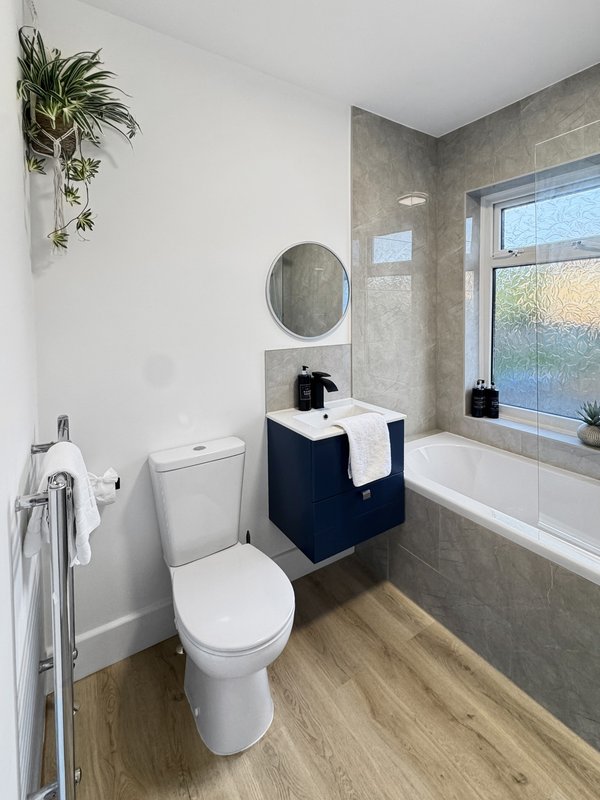 Modern bathroom with toilet, vanity sink, circular mirror, bathtub and hanging plant