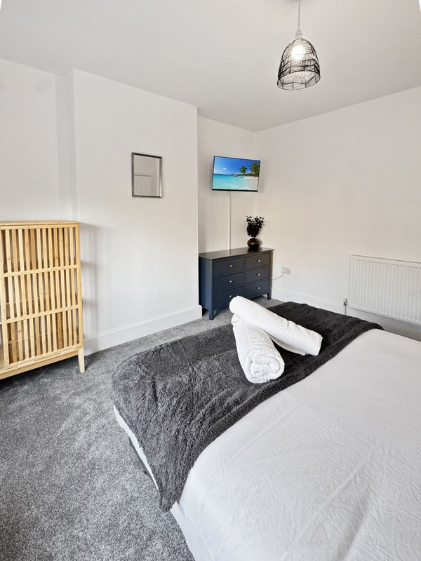 Modern bedroom with double bed, dark gray throw blanket, black dresser, wall-mounted TV, and pendant light
