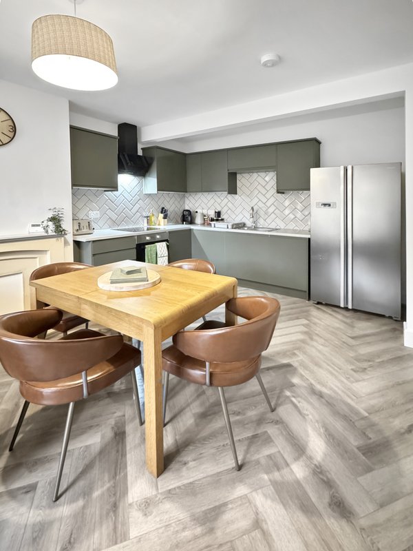 Modern kitchen with wooden dining table, brown chairs, olive cabinetry and stainless steel appliances