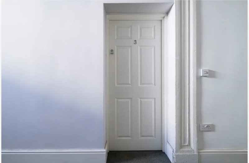 Hallway with white six-panel door, white walls, and light switch