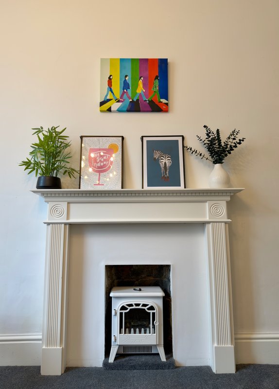 Fireplace with white mantel decorated with potted plants, framed artwork, and colorful wall art above