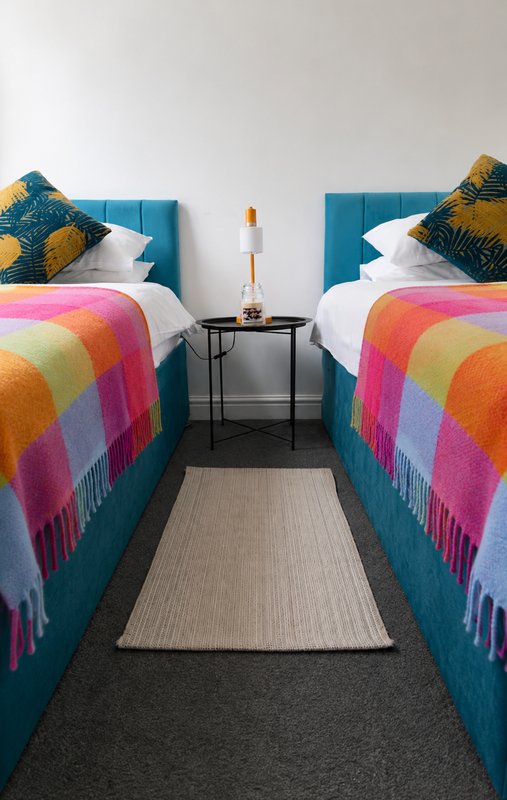 Twin bedroom with blue upholstered headboards, colorful patchwork blankets, and shared nightstand