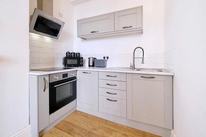 Modern white kitchen with built-in oven, sink, countertop appliances and wooden floor
