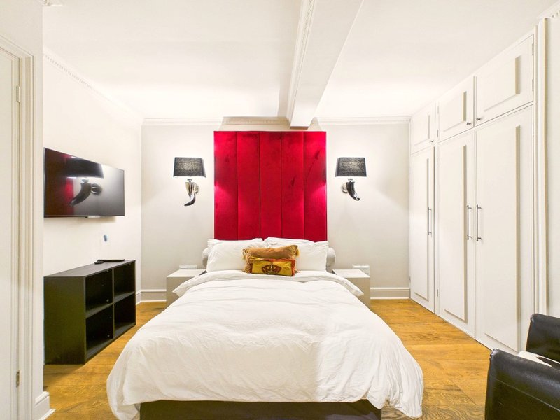 Modern bedroom with double bed, red fabric headboard, white bedding, wooden floor and wall lamps