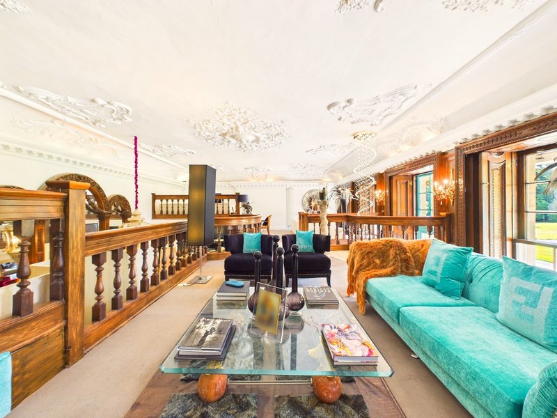 Spacious open-plan living area with turquoise sofa, wooden furniture, bookshelves, and large windows overlooking garden