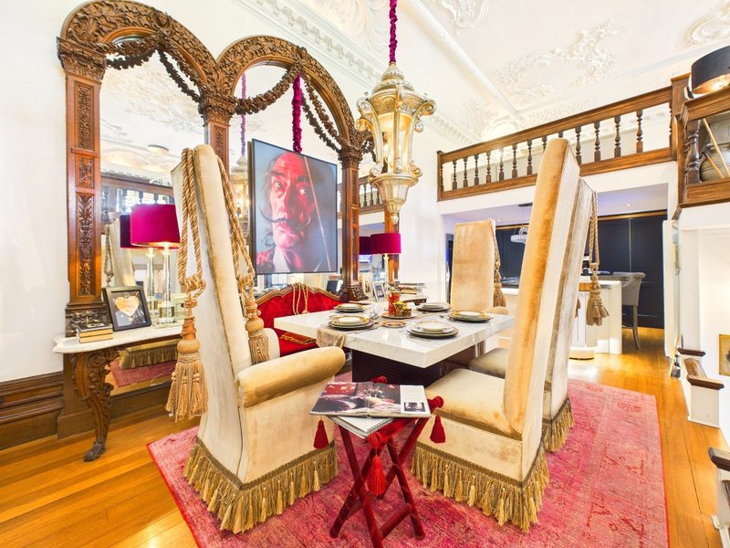Ornate dining area with gold-framed mirrors, upholstered chairs, red accents and wooden flooring