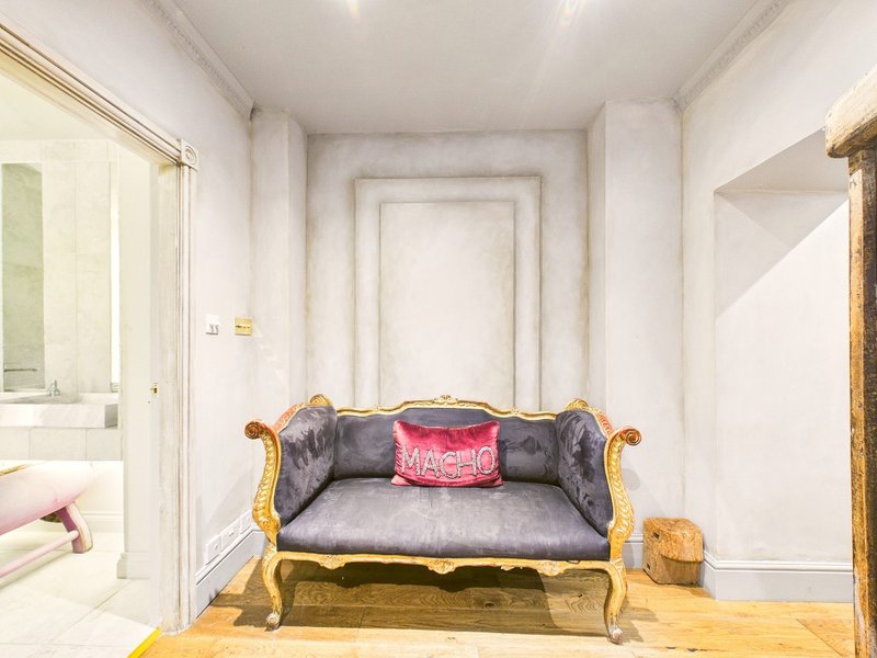 Ornate gilt-frame sofa with grey upholstery and pink cushion in bright white hallway