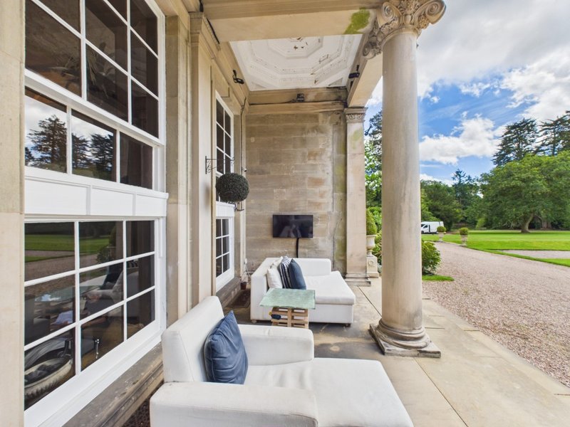 Covered veranda with white seating, stone columns, and manicured grounds visible
