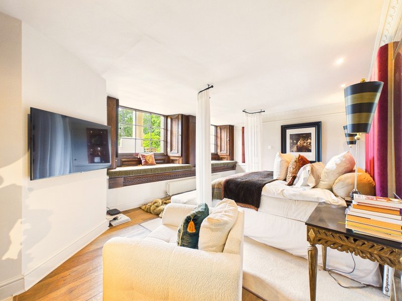 Bright modern bedroom with two beds, TV, windows, wooden floor and cushioned seating