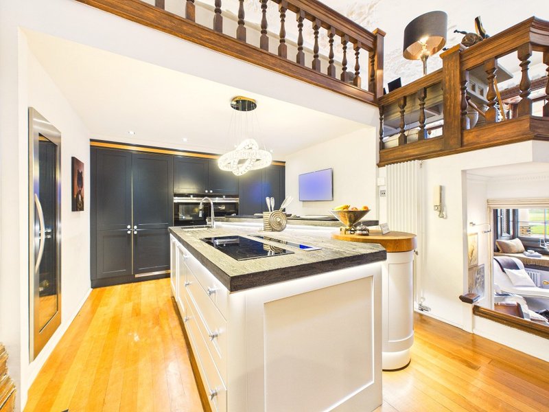 Modern kitchen with white cabinetry, dark countertop island, wooden flooring and mezzanine above