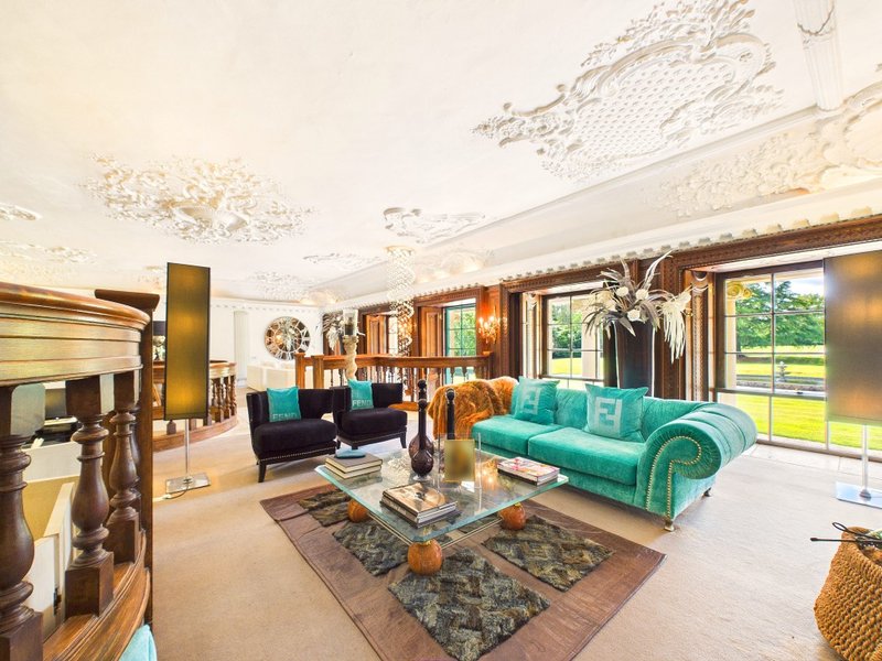 Spacious living room with turquoise sofa, fireplace, bookshelves and large windows overlooking garden
