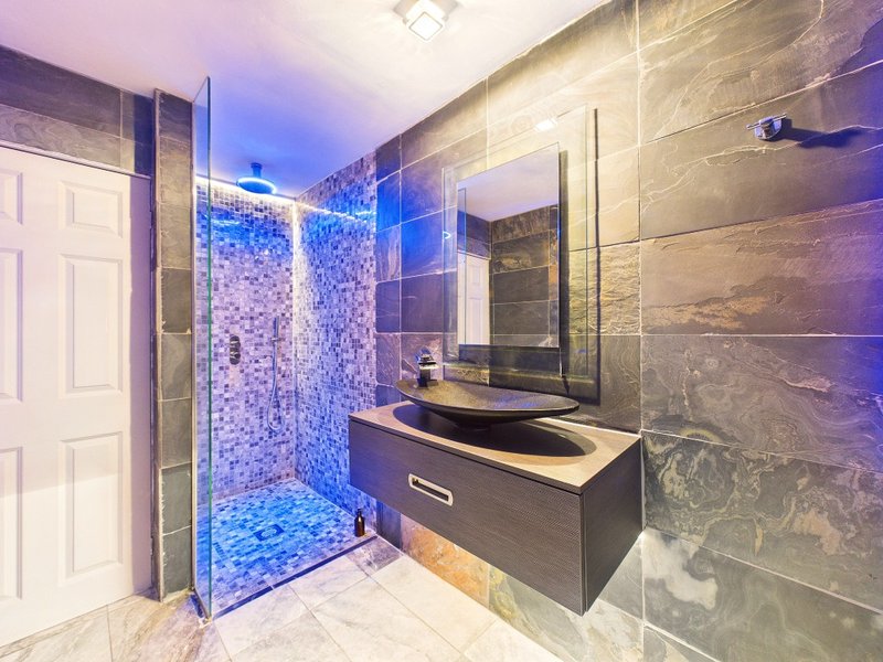 Modern bathroom with walk-in shower, dark vanity, dual sinks and blue LED lighting