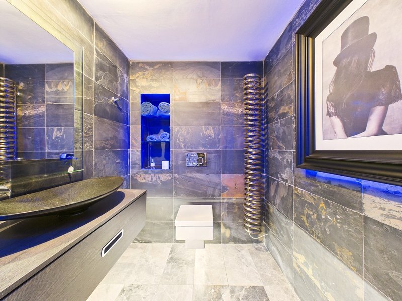 Modern bathroom with marble tiles, curved bathtub, glass shower enclosure and blue accent lighting