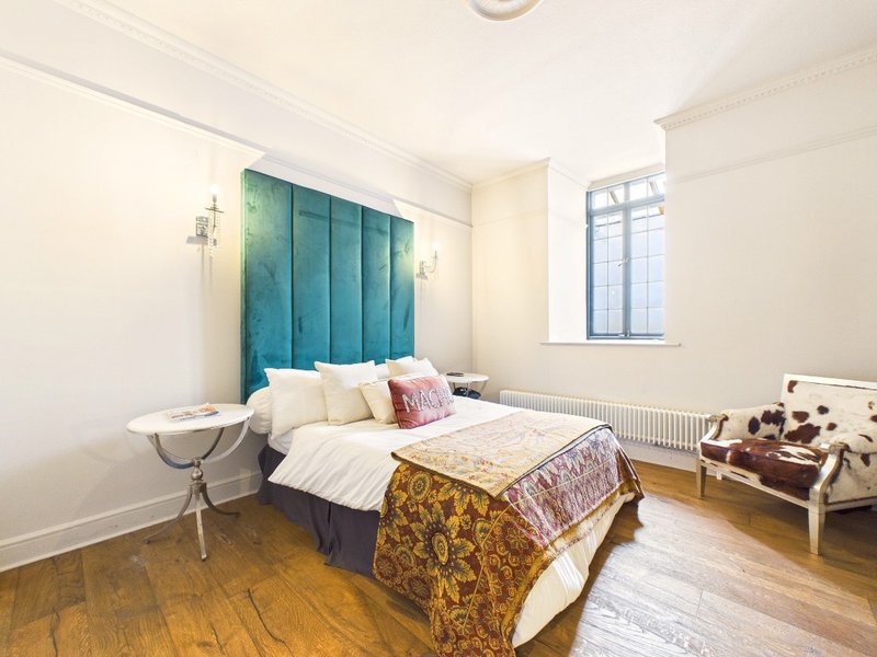 Bright bedroom with teal upholstered headboard, double bed, wooden floor and window