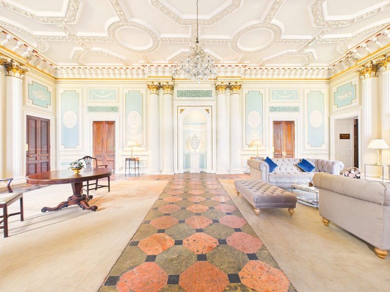 Grand neoclassical ballroom with ornate ceiling, crystal chandelier, patterned floor and period furniture