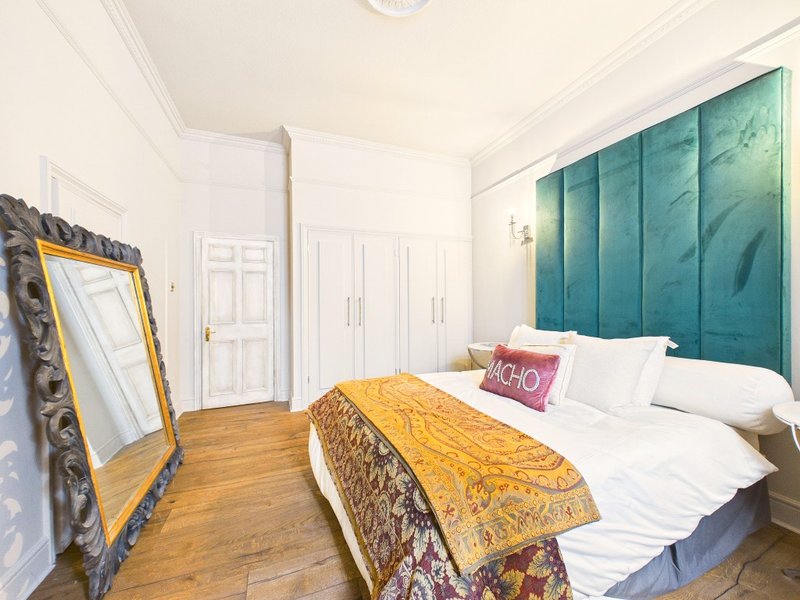 Bright bedroom with double bed, teal headboard, wooden floor, and gold-framed mirror