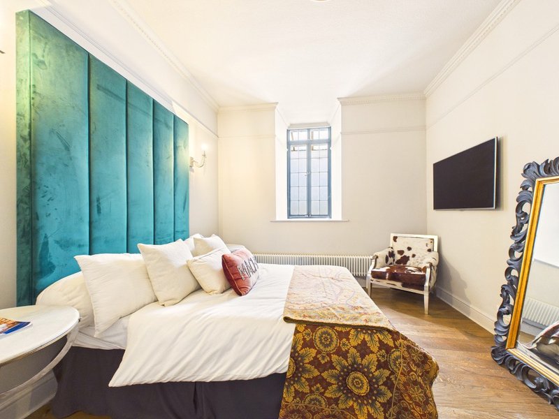 Modern bedroom with teal upholstered headboard, white bedding, wooden floor and wall-mounted TV