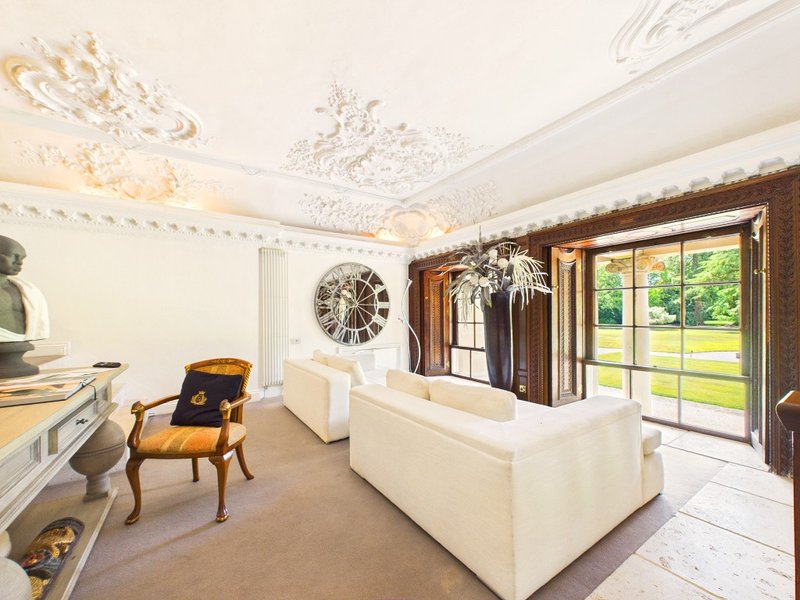 Spacious living room with cream sofa, ornate ceiling, wooden chair and French doors to garden