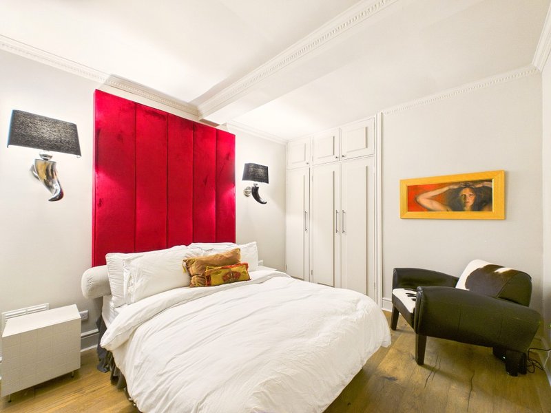 Modern bedroom with red velvet headboard, white bedding, wooden floor and wall art