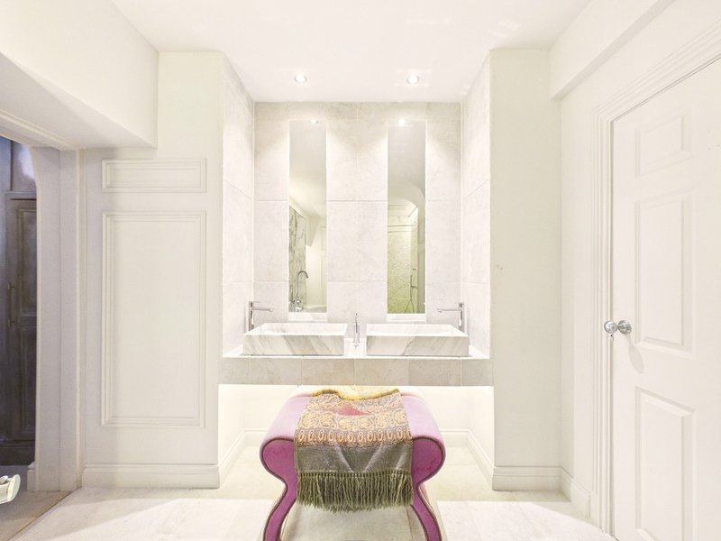 Modern bathroom with dual vanity, large mirror, white cabinetry and decorative purple chair