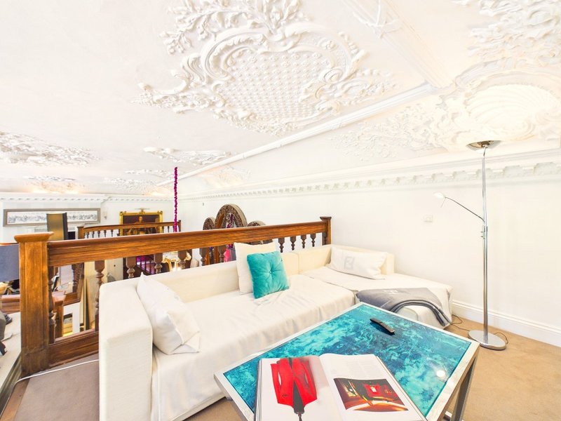 Bright attic bedroom with white sofa, turquoise cushion, wooden shelving and ornate ceiling