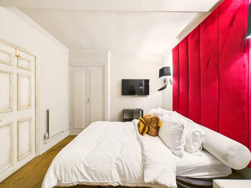 Modern bedroom with double bed, white bedding, red headboard and wall-mounted TV