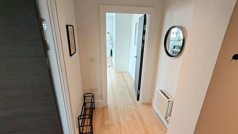 Modern hallway with wooden flooring, white walls, and multiple doorways with mirror