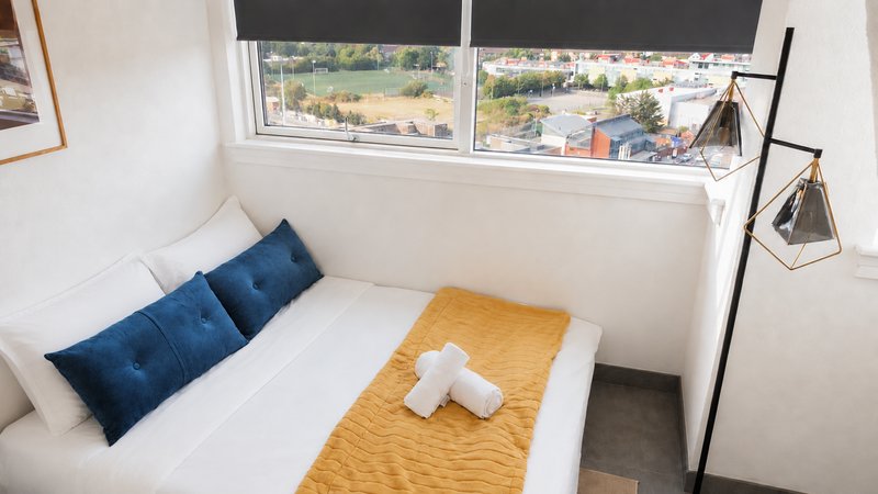 Bright bedroom with single bed, blue pillows, yellow throw, and large window overlooking landscaped grounds