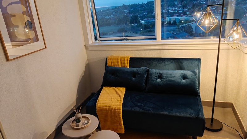Modern bedroom corner with black sofa, yellow accent pillows, pendant lights and city view window