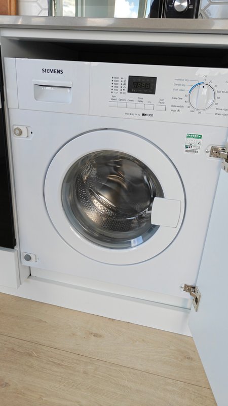 Built-in white Siemens washing machine in kitchen cabinetry with wooden floor