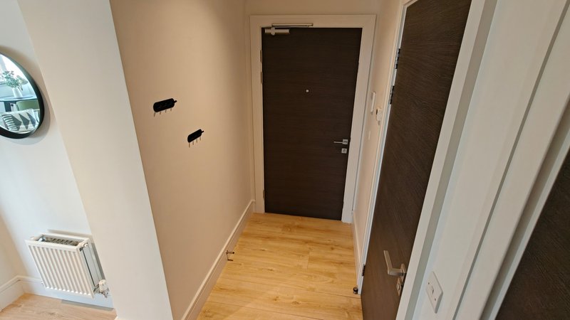 Hallway with wooden floor, beige walls, dark doors and white radiator