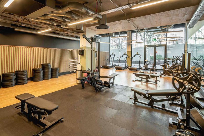Modern gym interior with exercise bikes, weight bench, dumbbells and industrial ceiling