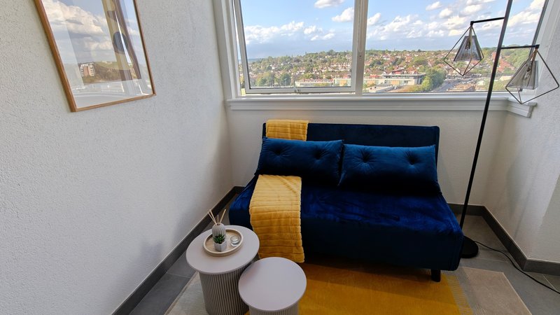 Modern bedroom with blue velvet sofa, yellow throw blanket, and large windows overlooking city landscape