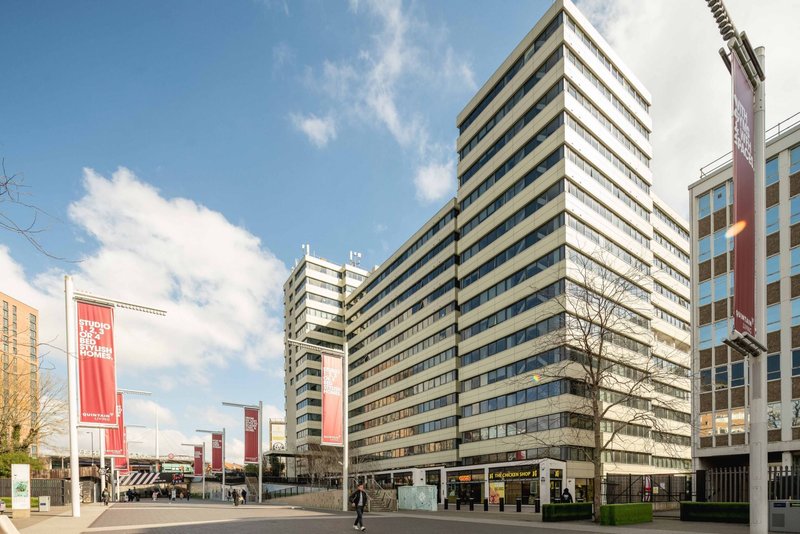 Modern multi-story residential building with striped facade, street-level shops and plaza area