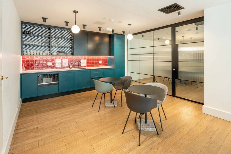 Modern kitchen and dining area with teal cabinetry, red tile backsplash, wooden flooring and three gray chairs